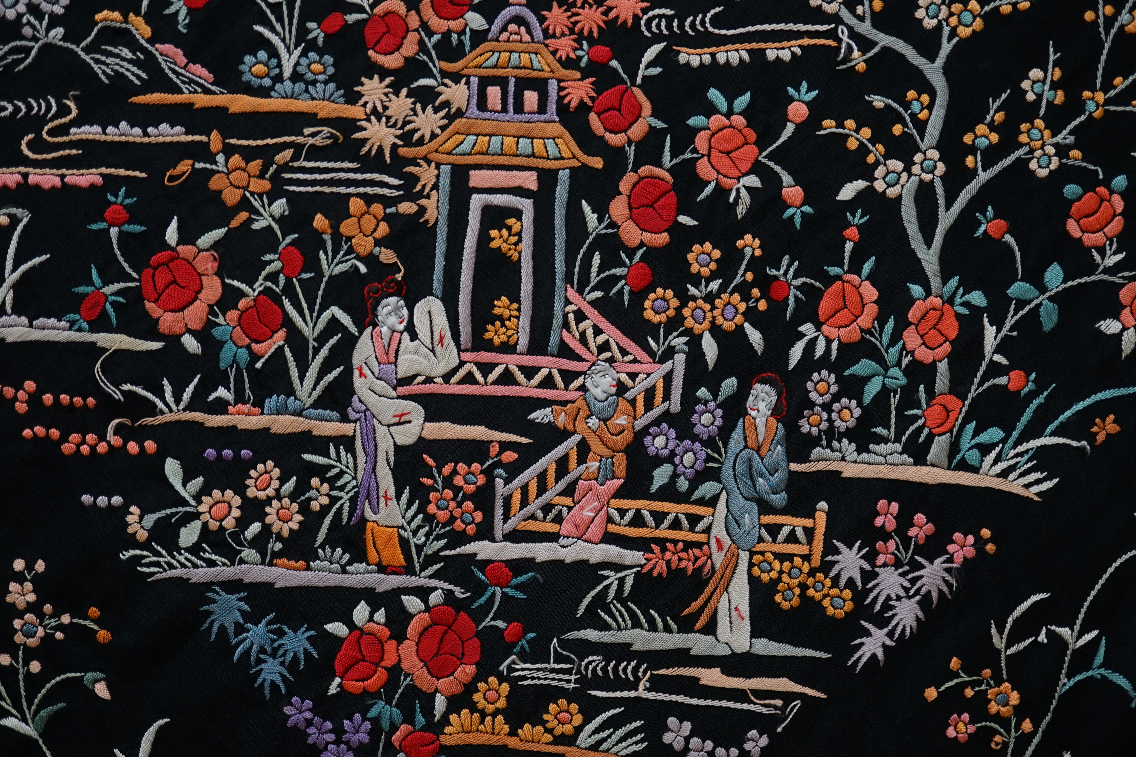 An early 20th century Chinese black silk shawl, with all over coloured floral embroidery, embroidered with multi-coloured silks and a long silk fringe, unusually the four corners are embroidered with a figurative pagoda